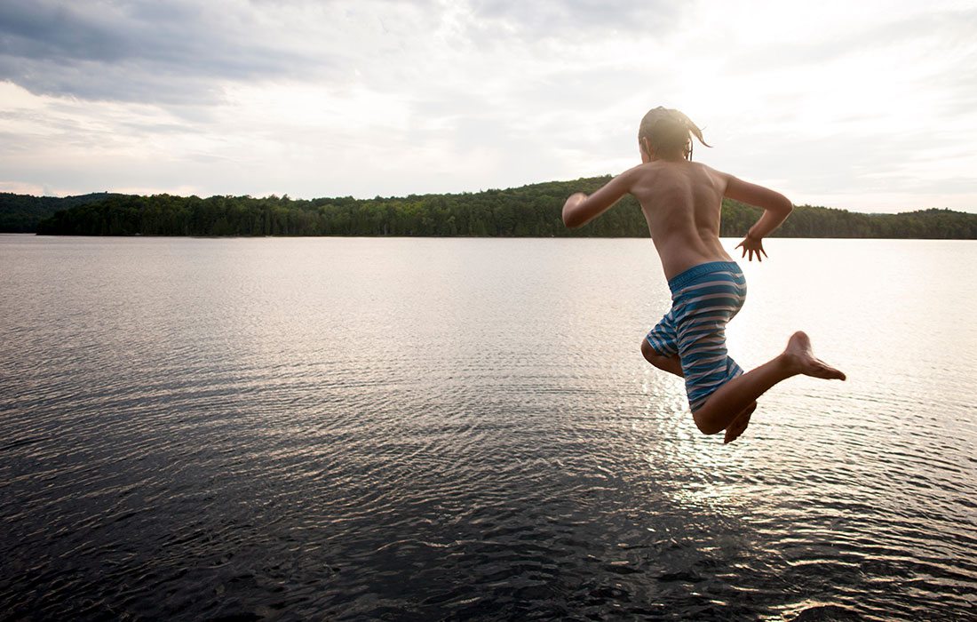 Boy in swim trunks in mid-air jumping into beautiful cove water