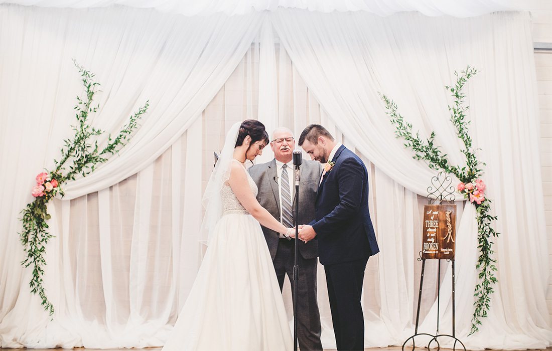 couple getting married with white backdrop with greenery