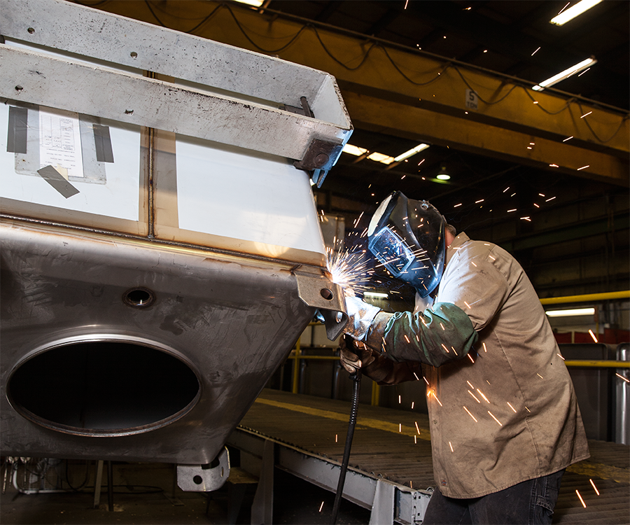 A welder adheres lifting lugs to the top of a Custom Metalcraft tank.