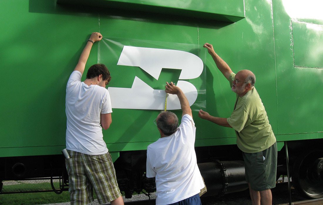 Ample Industries installing a printed label on the side of a train