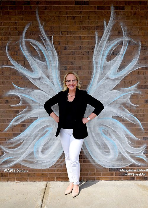 Carrie Arquitt of Arquitt Pediatric Dentistry in front of a mural by Andrea Ehrhardt in Springfield MO