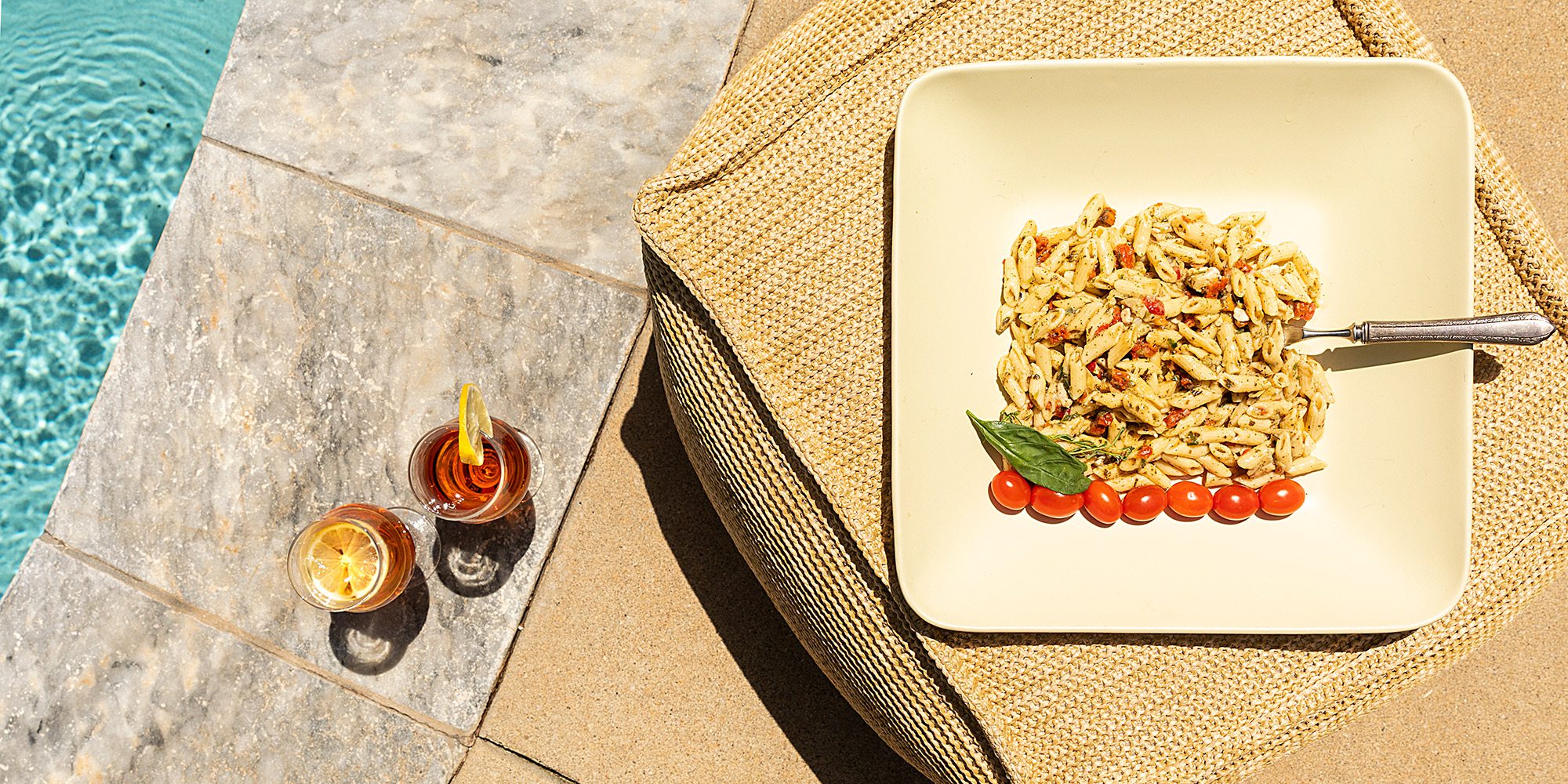 Summer pasta dish and iced tea with lemon next to an in ground backyard pool