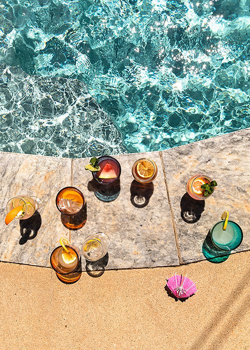Various cocktails next to an in ground backyard pool