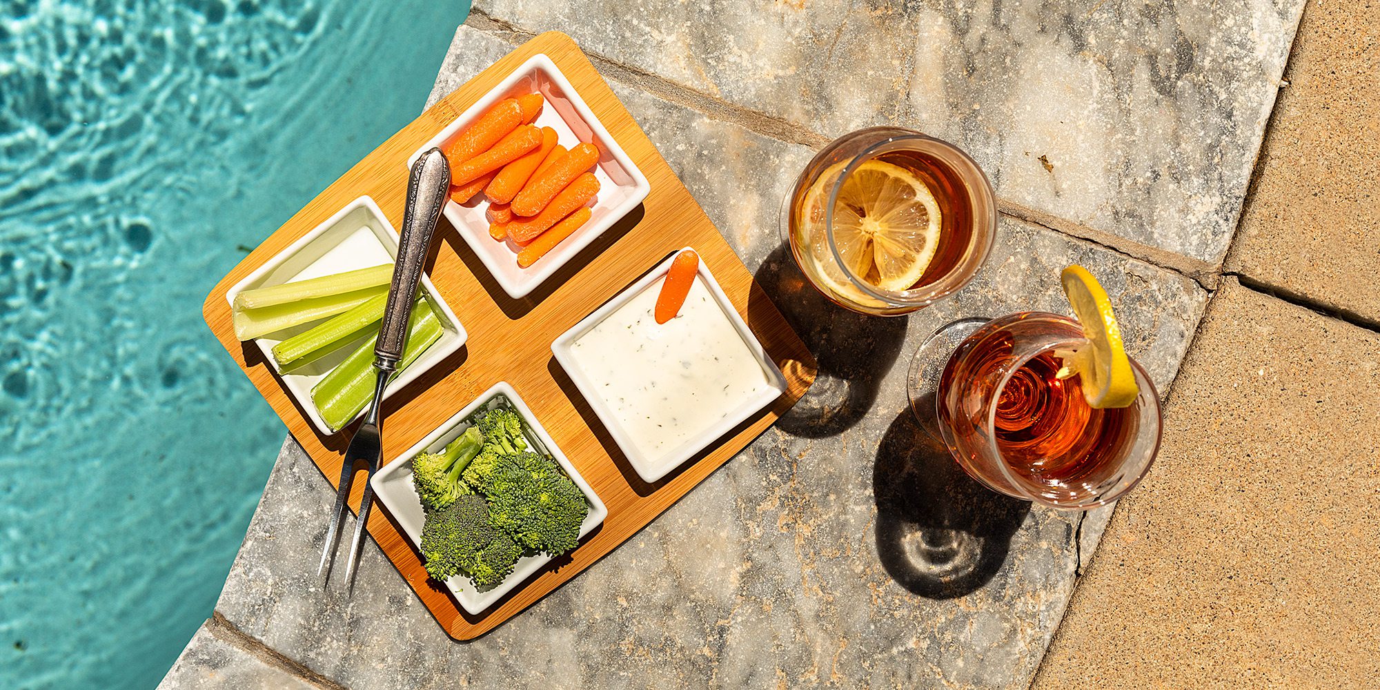 Veggie platter and iced tea with lemon next to an in ground backyard pool