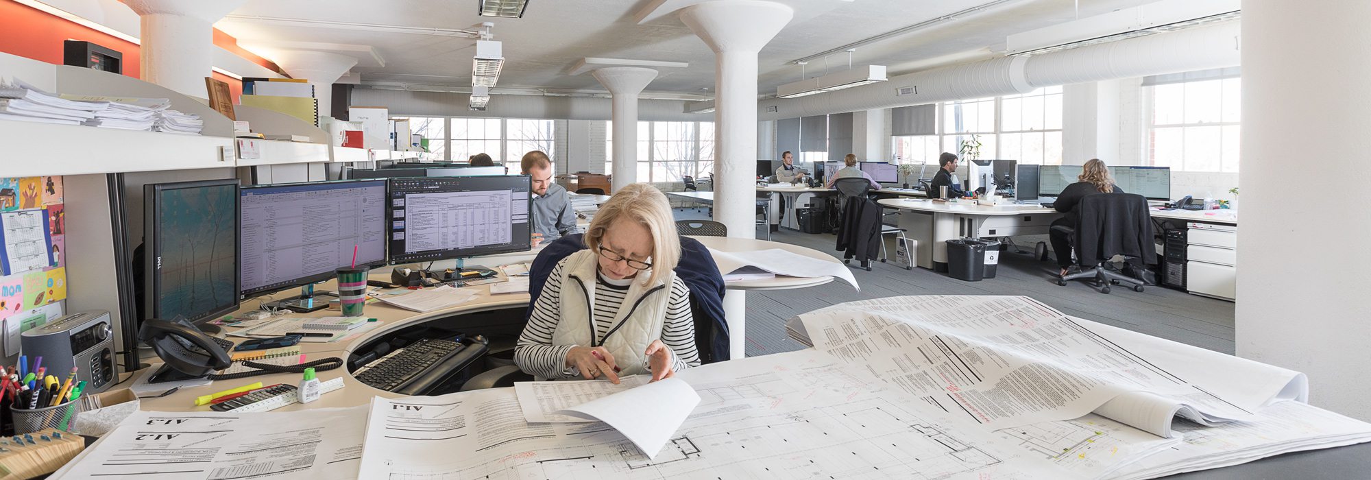 Woman working in open office with architecture plans on desk.