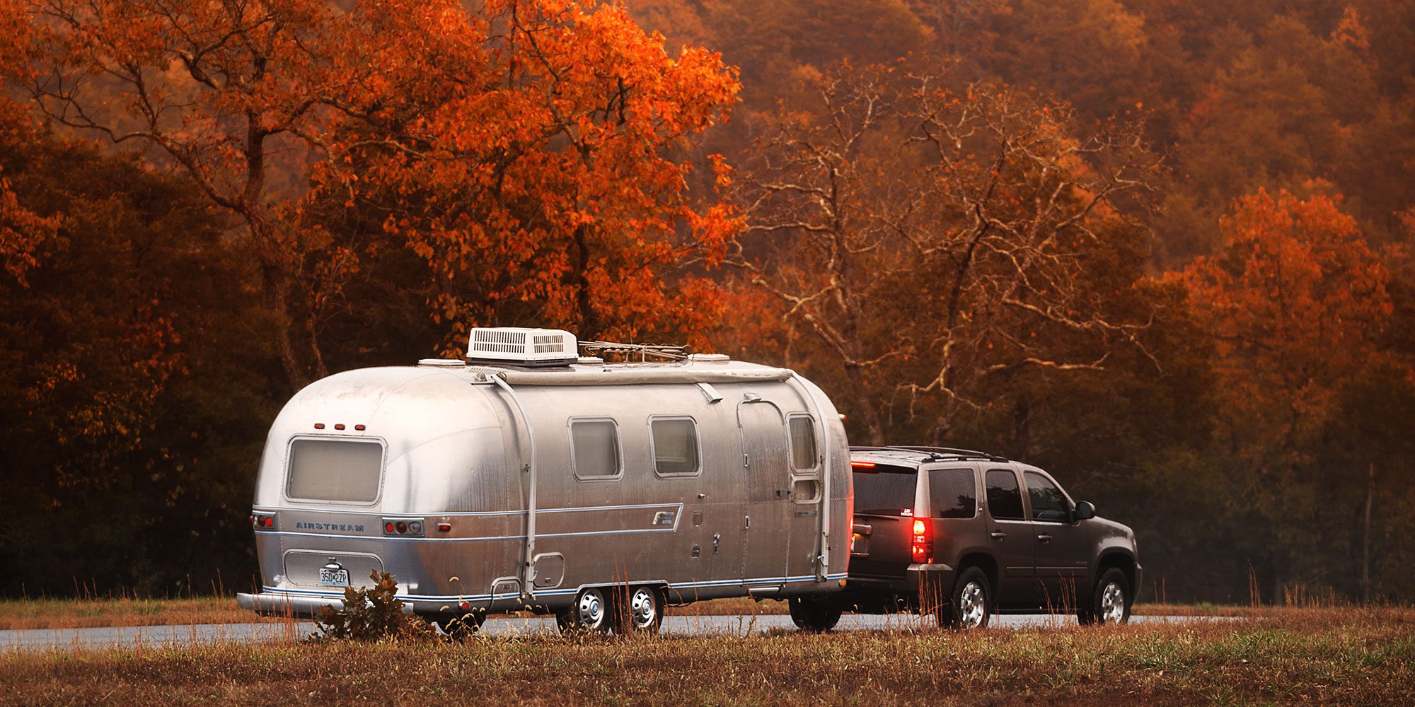 Silver Airstream being pulled down a scenic road with trees full of fall color