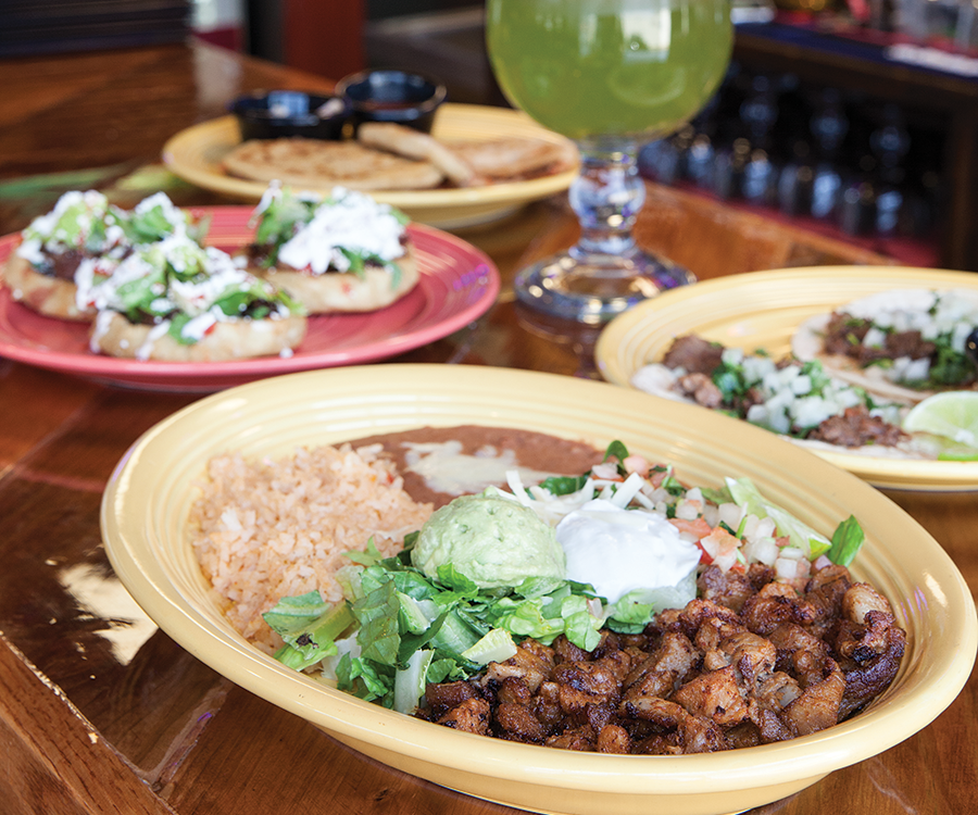 Mexican meal including sopes, rice and beans on bar with margarita.