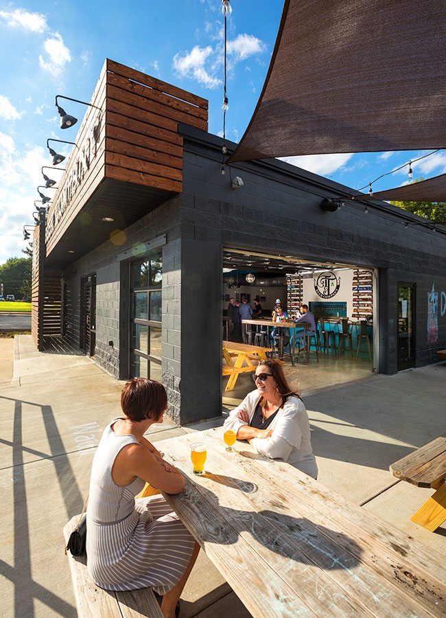 Two women drinking craft beers at a picnic table on Tie & Timber's outdoor patio