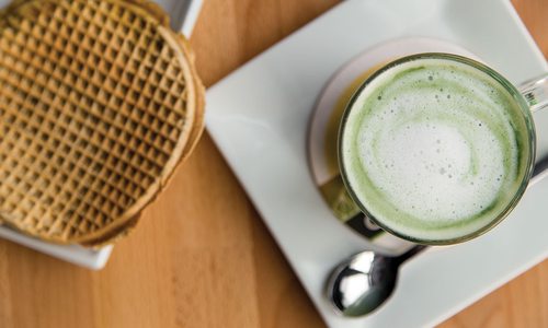 The Amsterdam Fog coffee sits on a white plate with a waffle on the side