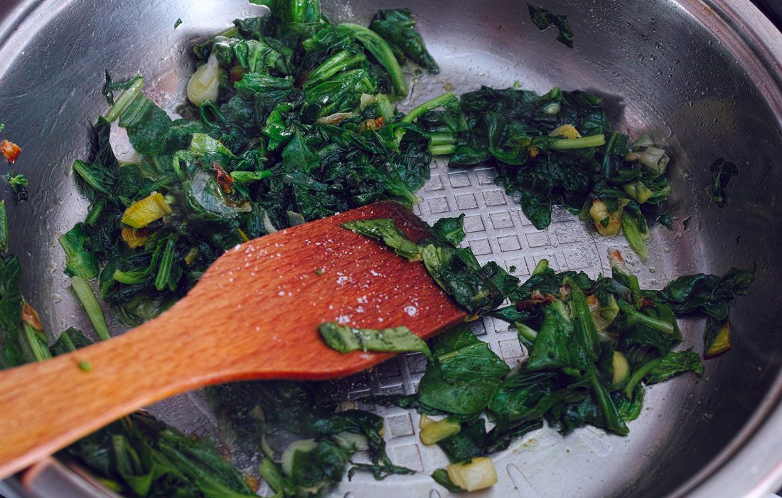 Fried spinach cooking with wooden spatula