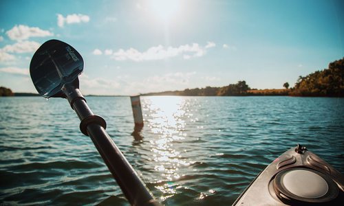 A kayak is raised out of the blue lake water reflecting the setting sun