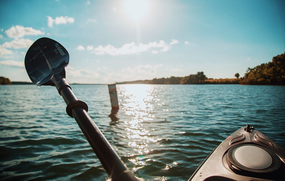 A kayak is raised out of the blue lake water reflecting the setting sun