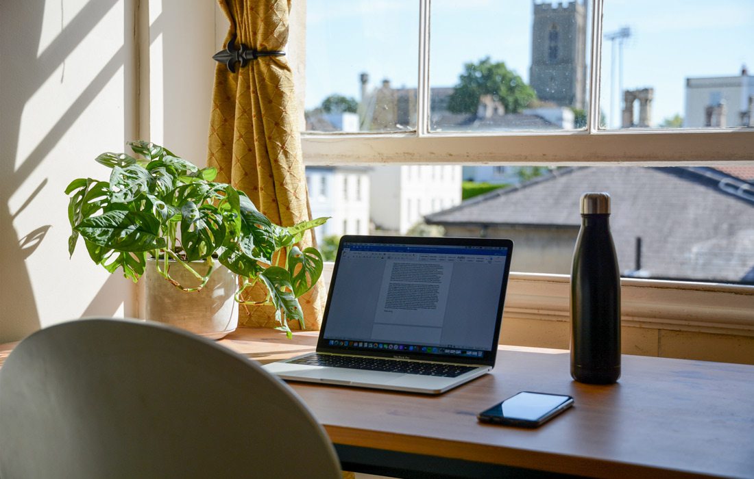 Laptop on desk beside window.