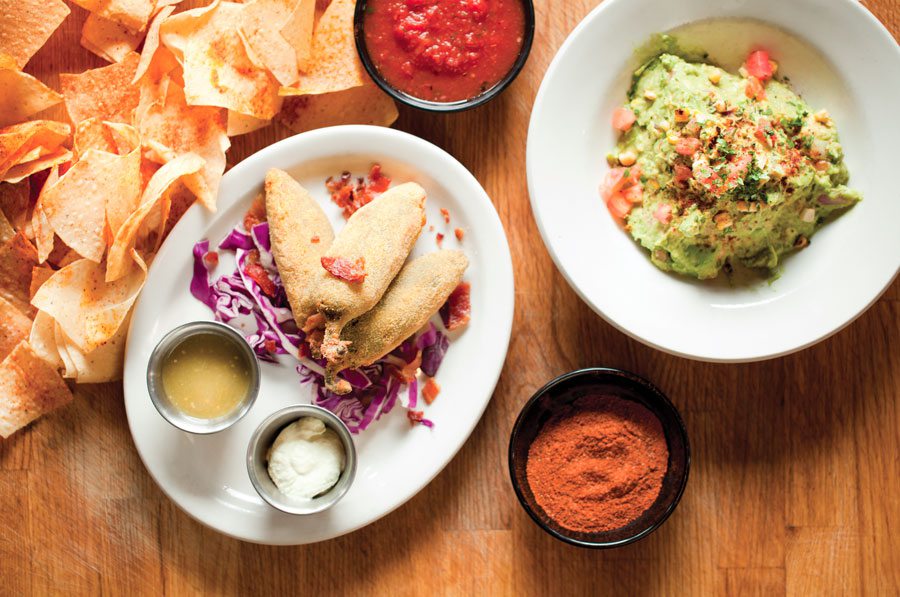 Chips and guacamole with salsas and stuffed jalapenos at a Mexican restaurant.