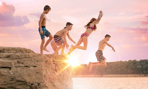 Family jumping off a bluff at Bull Shoals Lake at sunset