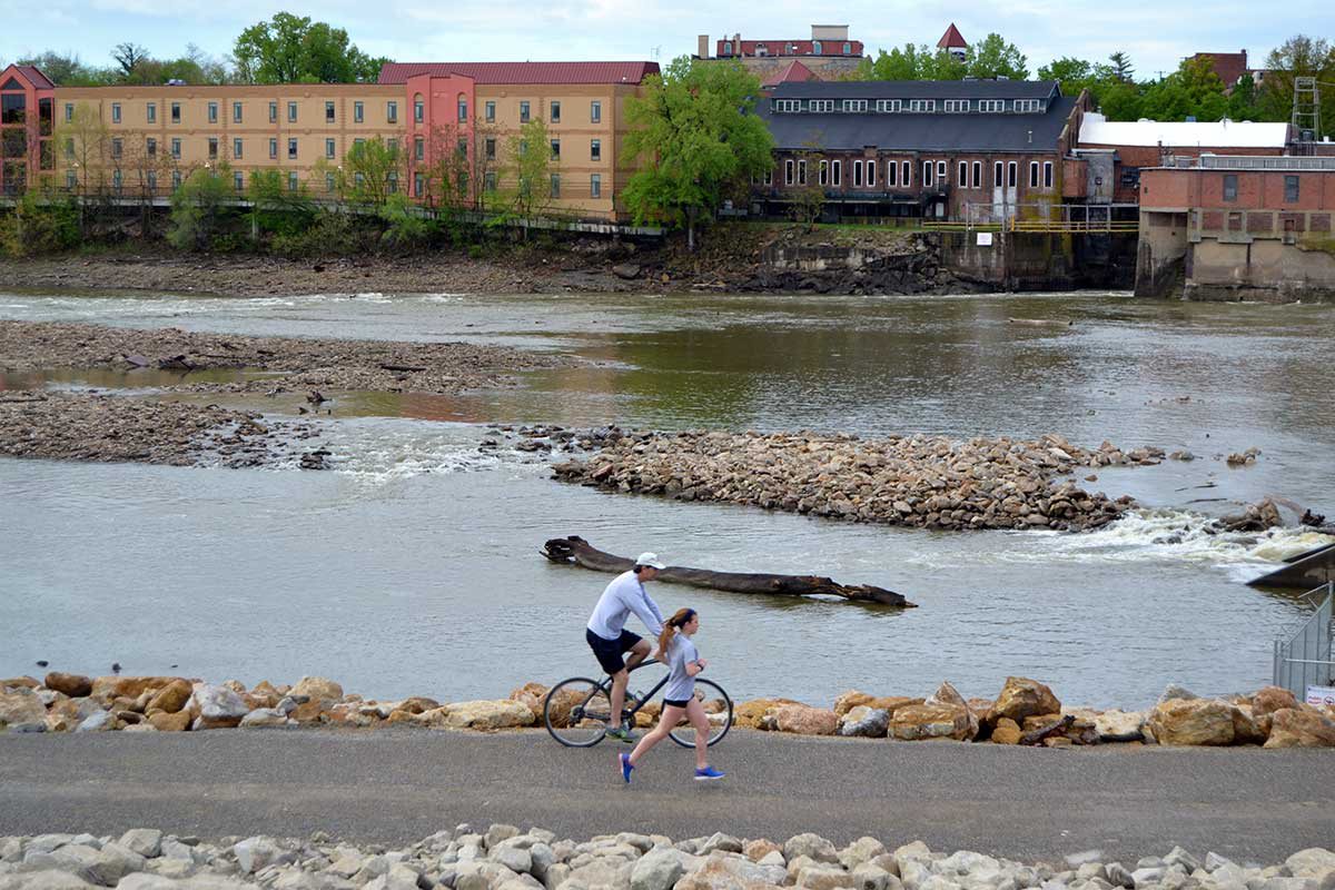 a woman runs and a man bikes along the river