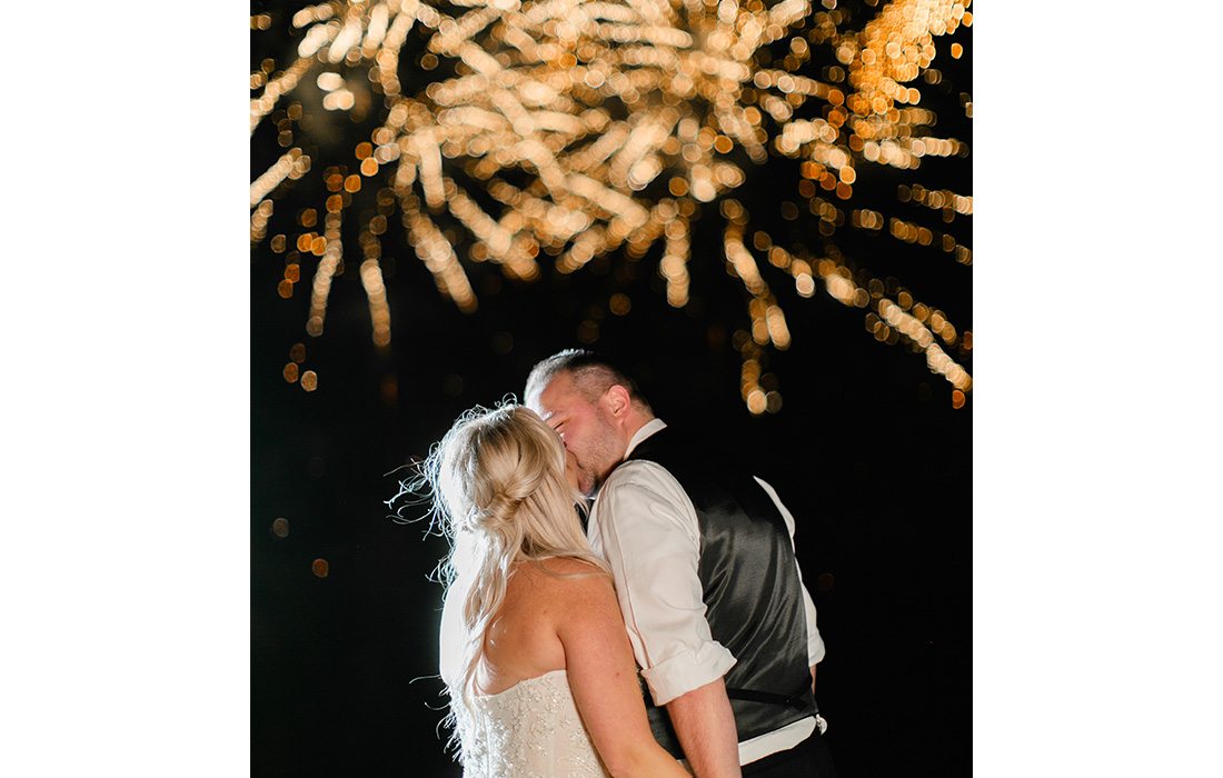 Bride and groom kissing during fireworks.