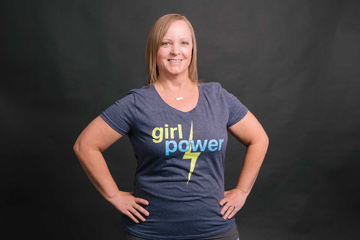 Shana stands with her hands on her hips, smiling in her "girl power" t-shirt