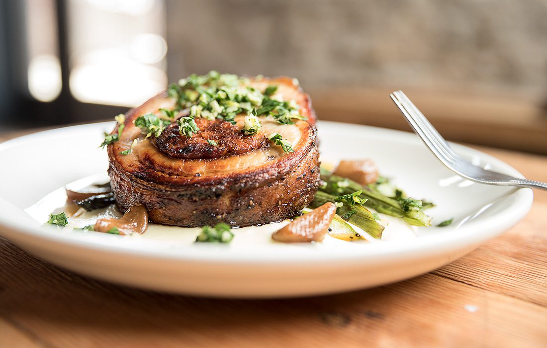 In the porchetta dish, parsnip and carrot cognac purees sit beneath a pork belly round.