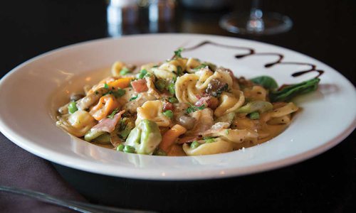 The different color pasta sits in a white bowl, brown sauce drizzled on the edge