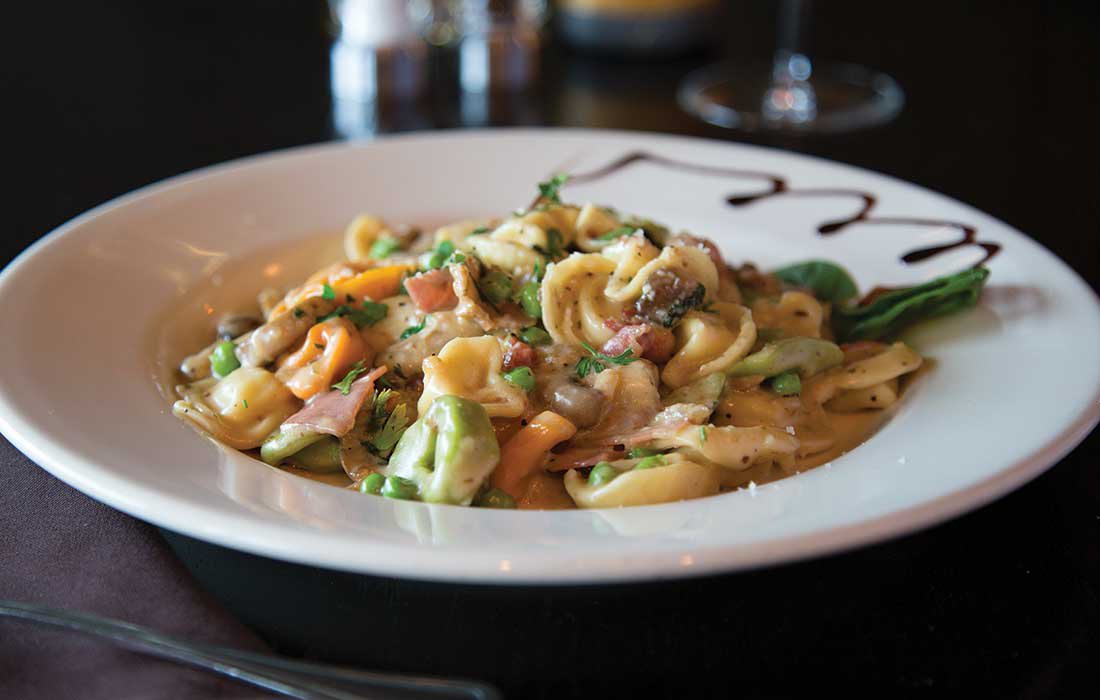 The different color pasta sits in a white bowl, brown sauce drizzled on the edge