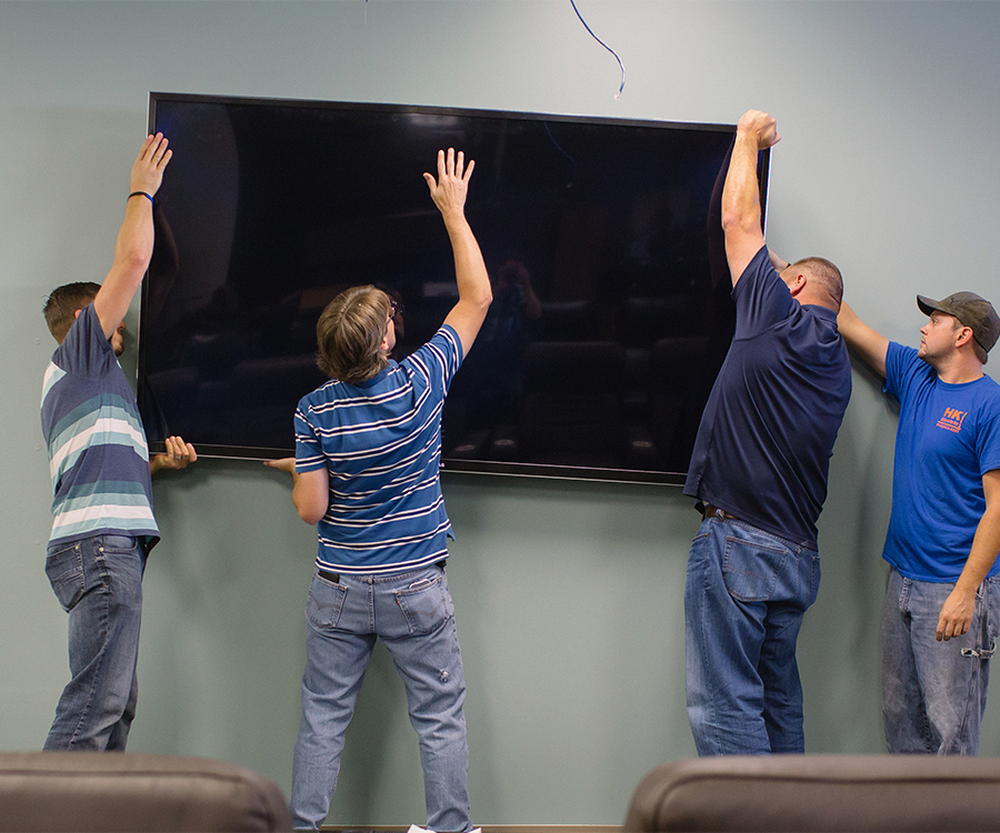 Employees Ryan Meredith, Michael Black and Michael Cory and Matthew Williams with HK Electric install an 85-inch TV at the PILR TECH office.