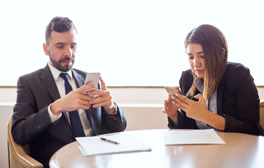 two people distracted by cell phones at work