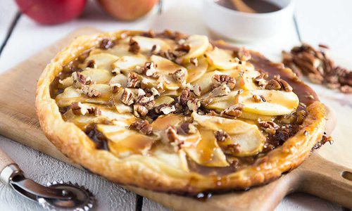 the circular pastry sits on a wooden serving platter, pecan scattered on top