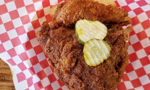 Chicken sandwich topped with pickles and sitting in a platter