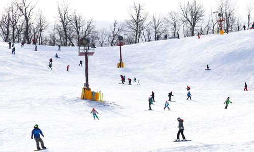 A crowd of people dressed in winter gear ski and snowboard down a snowy hill at Snow Creek Resort.