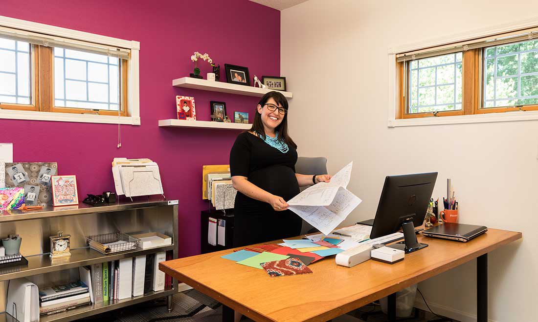 woman stands behind her desk smiling at the camera holding papers in her hand