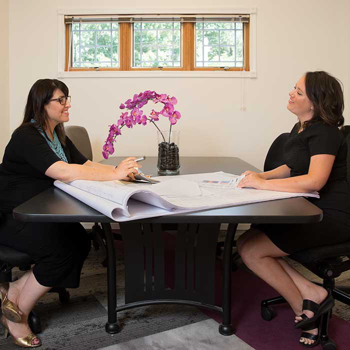 two women sit across from each other at a table with sheets of paper in front of them