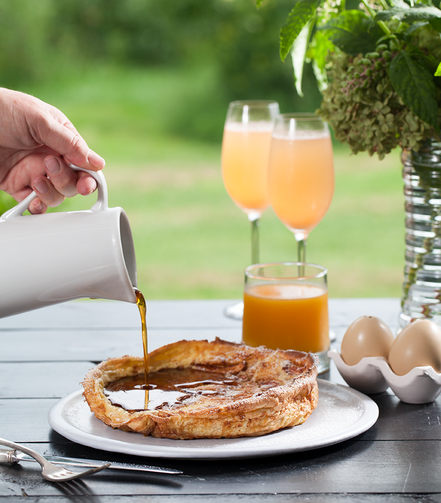 Pouring syrup on French toast with glasses of mimosas