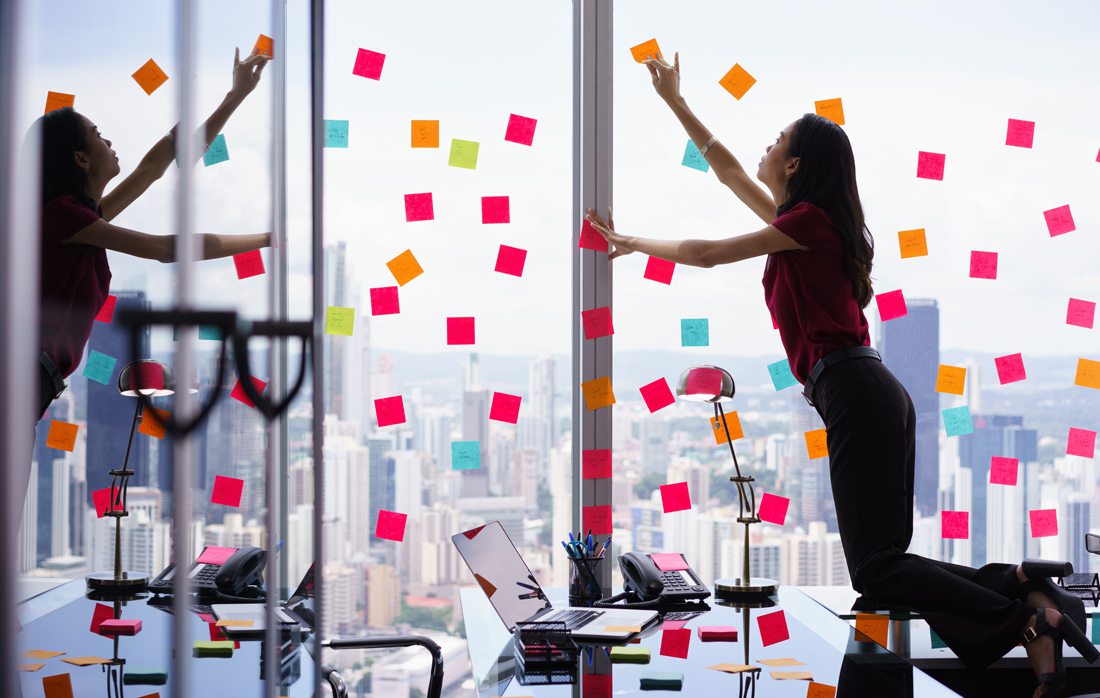 Woman working in skyscraper, putting sticky notes on windows.