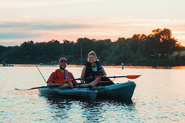 A man and a woman smile at the camera while floating in their kayaks