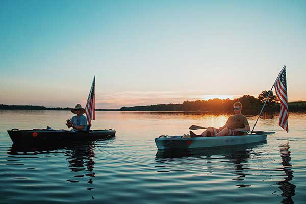 Two men sit in their boats with the sun setting past the water behind them