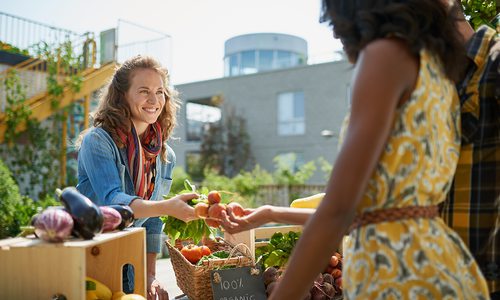 One woman hands produce to another woman at a farmers market