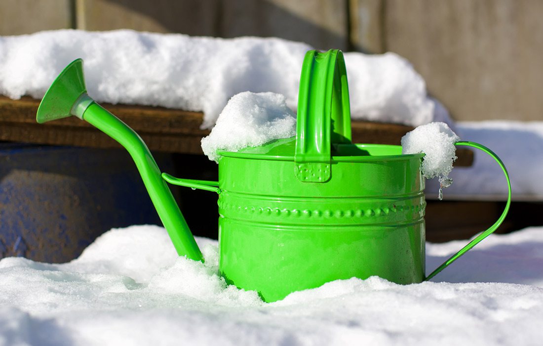 Green watering can sitting out in the snow stock image