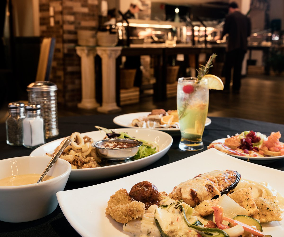 Table filled with Italian food including chicken Parmesan, sausage and peppers, chicken Alfredo and toasted ravioli