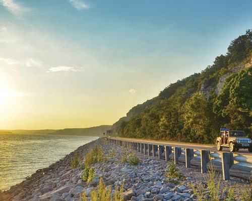 a road stretches between a forest cliff side and the coast